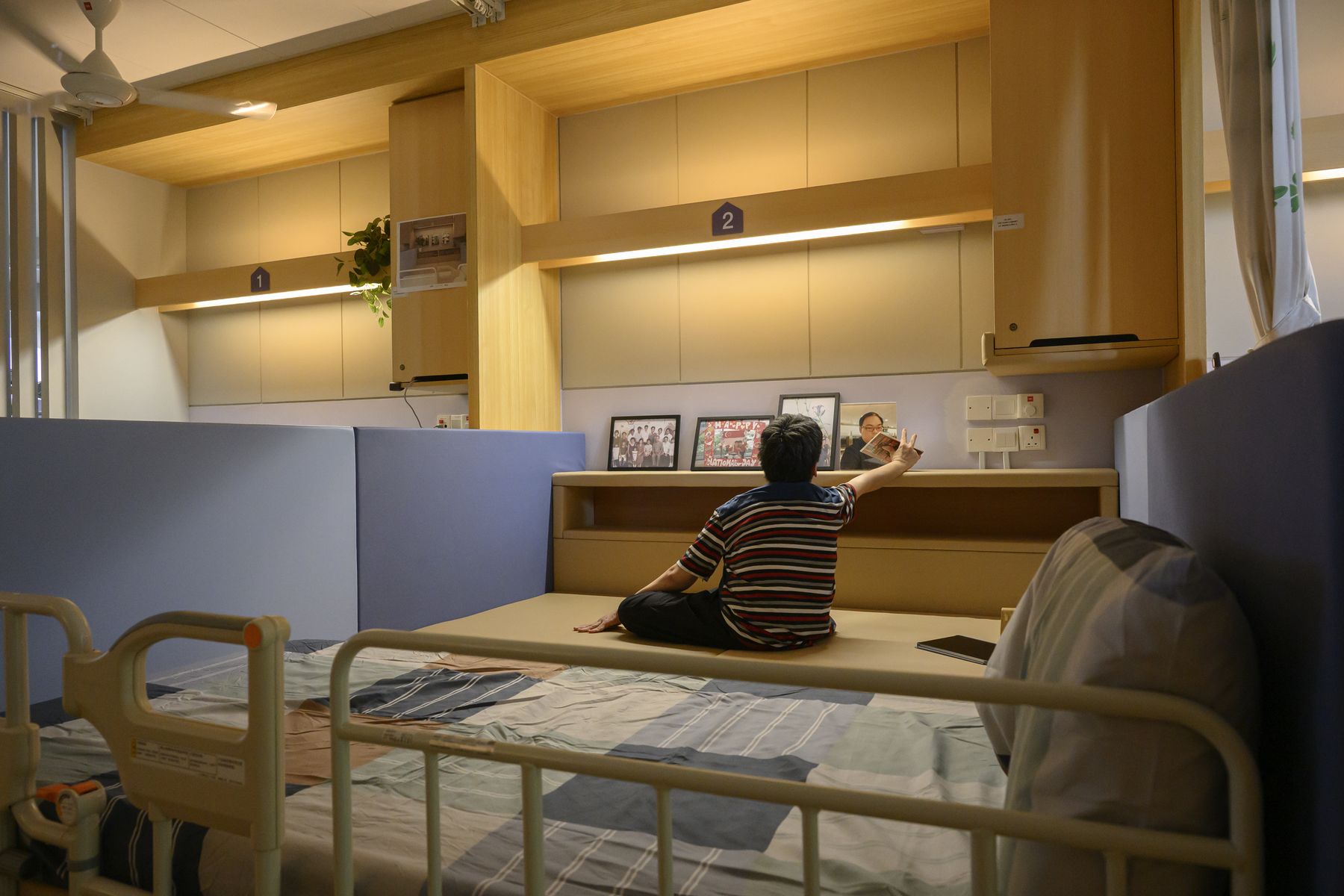 A resident sitting on the floor-based bed, reaching up to the shelf above