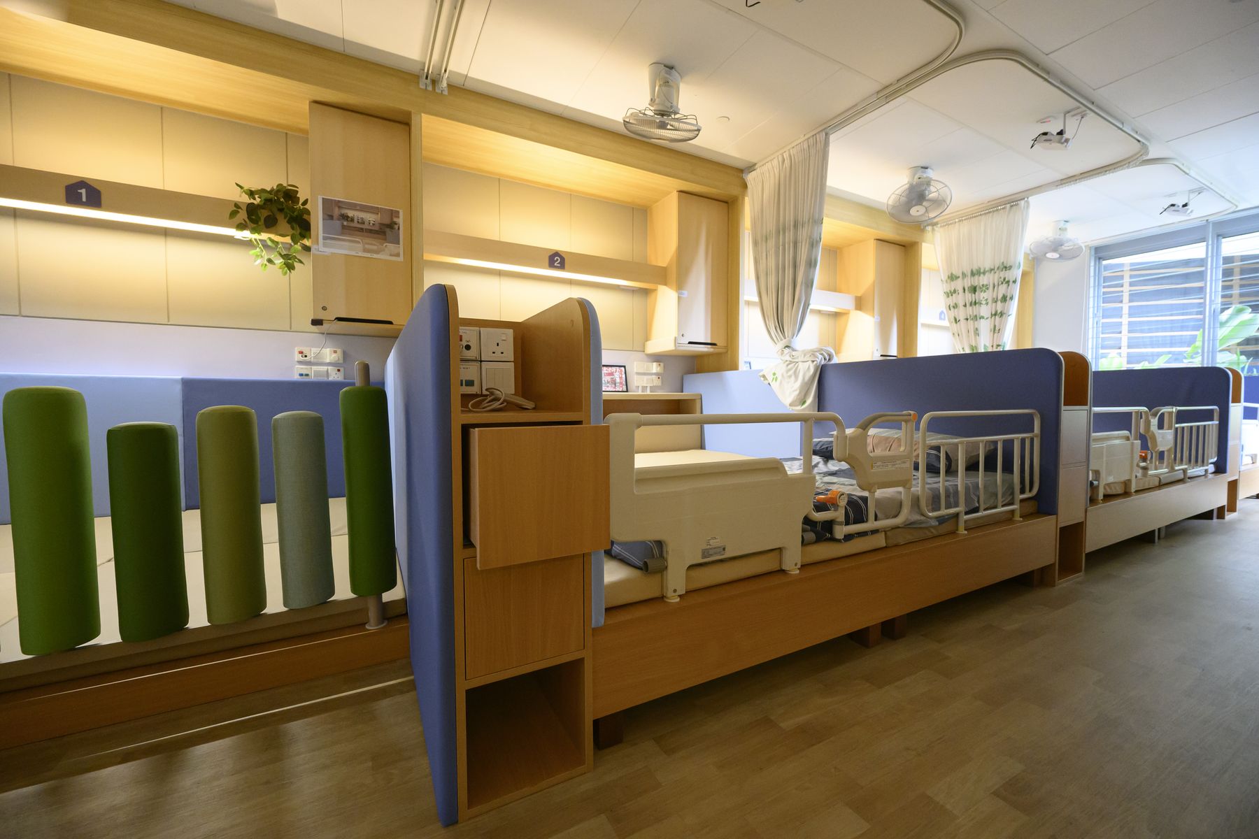 The ward from the entrance: bolster dividers, floor-based bays and a hospital bed kept for care