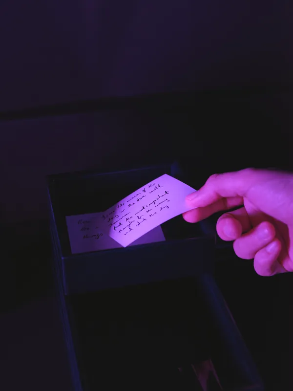A hand placing a handwritten note into a small black box